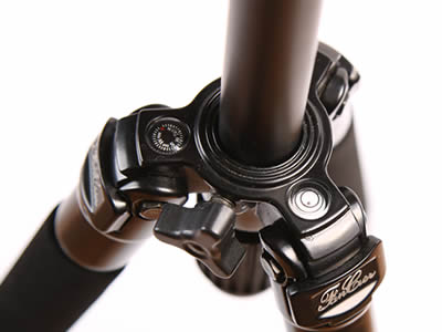 A camera tripod standing on the white background with a glass circular bubble level vial on it.